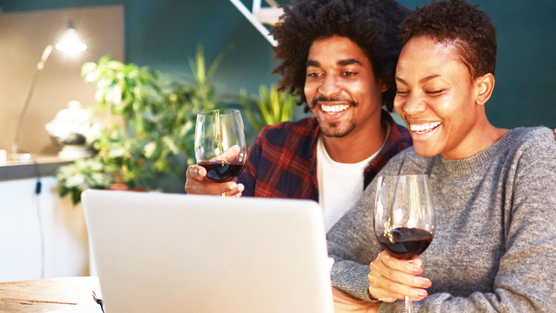 two people sitting holding galsses of wine and a laptop in their front